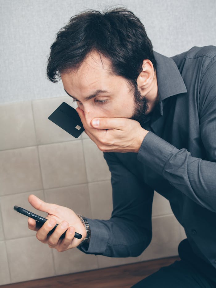 Man in shock discovering possible fraud or data breach with smartphone and credit card.